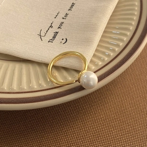 Macro shot of an elegant gold open ring featuring a lustrous white pearl on a ceramic tray