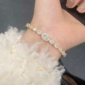 Dettaglio di elegante bracciale dorato con zirconi ovali su manica di pelliccia bianca