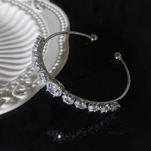 Dettaglio di un bracciale a C in argento con zirconi scintillanti su sfondo nero lucido