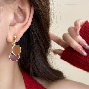 Détail de boucles d'oreilles pendantes circulaires marron et bordeaux portées par un mannequin