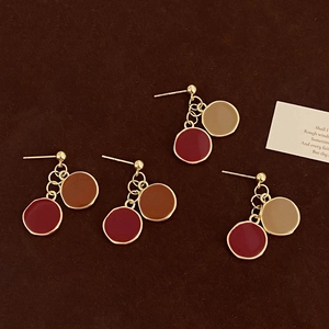 Gros plan de boucles d'oreilles pendantes en émail marron et rouge sur fond texturé