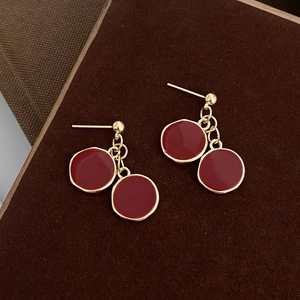 Détail de boucles d'oreilles pendantes en émail rouge et doré sur fond marron