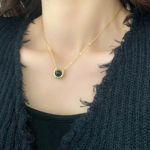 Detail of horseshoe pendant with black pearl on gold chain over black knit sweater