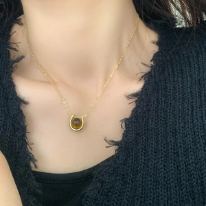 Close-up of a gold U-shaped necklace with a brown tiger eye stone on a black outfit
