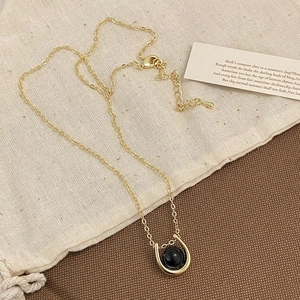 Detail of a gold U-shaped necklace with a black stone on a minimalist linen bag