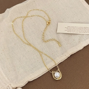 Detail view of a gold-plated horseshoe pendant with a pearl on a soft fabric background