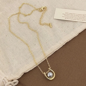 Detail of gold horseshoe pendant with grey pearl on textured linen and wood background