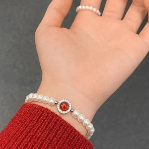 Détail de l'ensemble bracelet et bague en perles avec pierre rouge sur manche de pull rouge