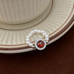Détail d'une bague en perles vintage avec une pierre rouge centrale et halo brillant