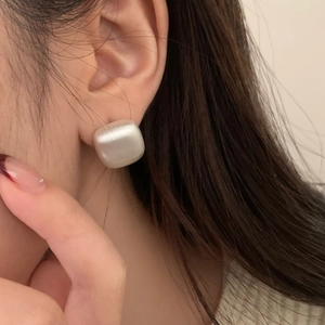 Macro shot of minimalist square matte pearl stud earrings on model with satin finish