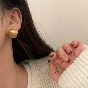 Close-up of minimalist gold square matte metal stud earrings worn by a female model