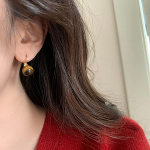 Gros plan de boucles d'oreilles vintage en œil de tigre et crochets dorés sur un modèle