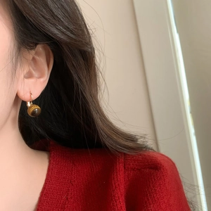 Gros plan sur des boucles d'oreilles vintage en œil de tigre et monture dorée sur modèle