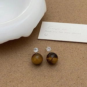 Détail de boucles d'oreilles œil de tigre avec cristal sur fond de papier kraft brun