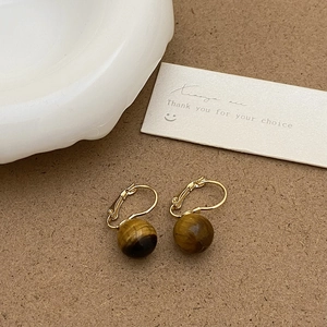 Gros plan de boucles d'oreilles en œil de tigre vintage avec crochets dorés sur fond brun