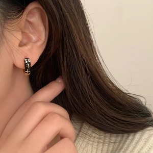 Detail of black enamel hoop earring with golden cross and sparkling zircon crystals
