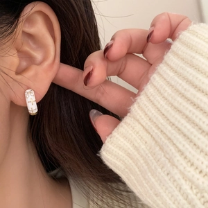 Detail of white enamel hoop earring with gold star motif and zircon stone on ear