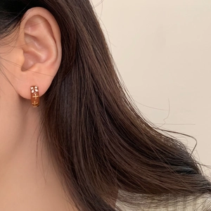 Close-up of brown enamel hoop earring with gold cross flower and zircon accents
