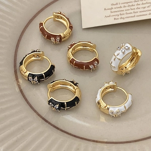 Close-up of enamel hoop earrings with gold finish and zircon cross details on a ceramic dish