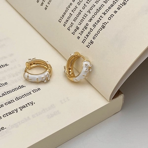 Detail of gold hoop earrings with white enamel cross pattern on a vintage book