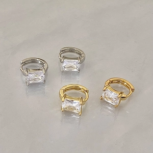 Orecchini a cerchio in oro e argento con zircone quadrato esposti su base grigia liscia