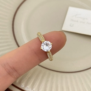 Minimalist gold ring with round cubic zirconia and pavé stones on a textured plate