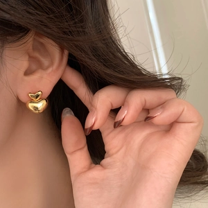 Close-up of elegant double layered gold heart earrings worn on ear showing high polish finish