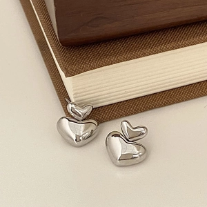 Macro shot of silver stacked double heart stud earrings on a textured book surface