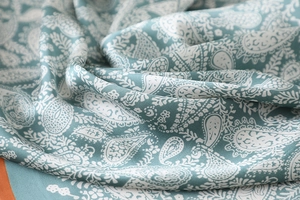 Macro shot of teal paisley silk scarf fabric showing glossy satin texture and drape