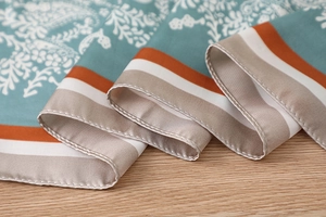 Macro detail of teal paisley silk scarf featuring elegant orange striped borders