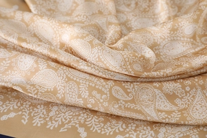 Macro shot of paisley pattern on champagne gold satin silk scarf showing soft texture
