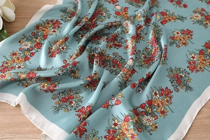 Detailansicht eines graublauen Seidenschals mit Blumenmuster und weißem Rand auf Holz