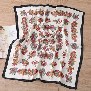 Nahaufnahme des Seidenschals mit Blumenmuster, schwarzen Rändern auf hellem Holzhintergrund