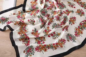 Detailaufnahme von Blumenseidenschal mit schwarzen Satinkanten auf Holzoberfläche