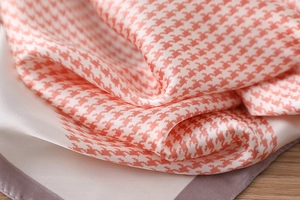 Macro detail of houndstooth silk scarf showing orange and beige fabric texture