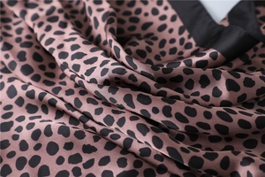 Gros plan d'un foulard en soie synthétique mauve à imprimé léopard avec bordure noire