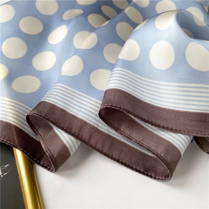 Vue détaillée d'un foulard en satin bleu clair à pois blancs et ourlet marron