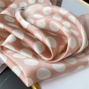 Gros plan d'un foulard en soie rose à gros pois blancs et détails de rayures