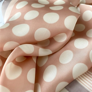 Détail d'un foulard en soie corail à gros pois, bords rayés et finition satinée