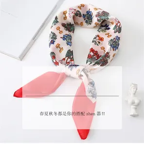 Detail of pink silk-feel scarf with floral and chain patterns on a flat lay surface