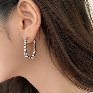 Boucles d'oreilles créoles perlées argentées au design géométrique portées par un mannequin
