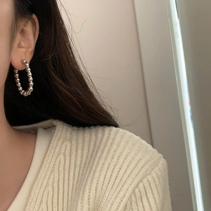 Gros plan de créoles perlées argentées portées par un mannequin au style minimaliste