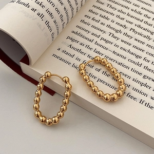 Détail de boucles d'oreilles créoles ovales perlées dorées sur un livre anglais ouvert