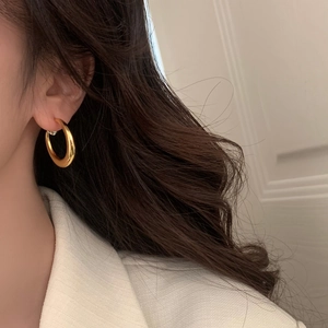Gros plan de boucles d'oreilles créoles dorées sur un modèle en blazer blanc