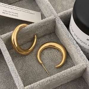 Détail des boucles d'oreilles créoles dorées épaisses sur un plateau à bijoux en velours gris