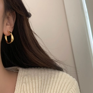Détail d'une boucle d'oreille dorée en forme de C portée avec texture métallique brillante