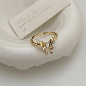 Détail d'une bague papillon dorée avec zircons bleus et violets sur assiette blanche