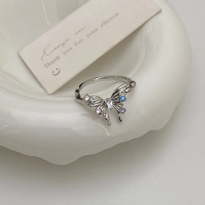 Détail d'une bague papillon argentée ornée de zircons colorés sur une assiette en céramique