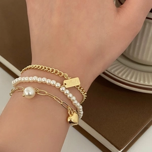 Three-layer gold chain bracelet set with pearls and heart pendant on model's wrist