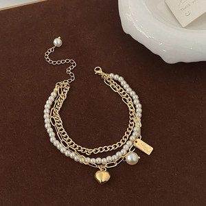 Minimalist multi-layer gold chain pearl bracelet with heart pendant on vintage background